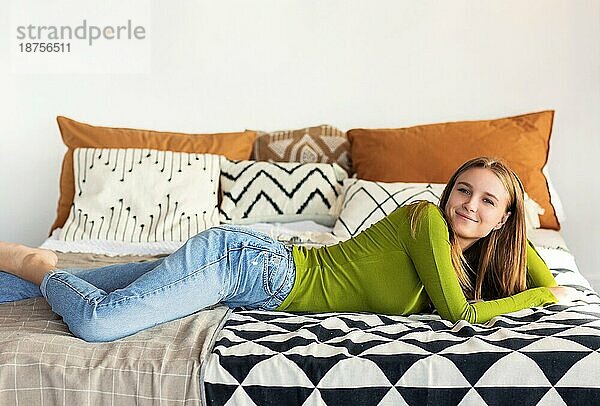 Lächelnde positive Teenagermädchen in lässiger Kleidung liegen auf dem Bett in ihrem gemütlichen Zimmer zu Hause  Ruhe nach der Universität  schöne junge Frau im Schlafzimmer entspannen  verbringen freie Zeit allein