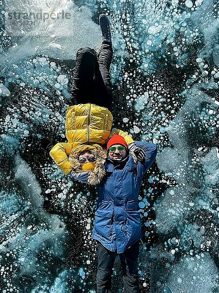 Glückliches Paar auf dem zugefrorenen Baikalsee in Winterkleidung. Transparentes Eis. Reisen im Winter  aktive Erholung  Sport  Urlaub