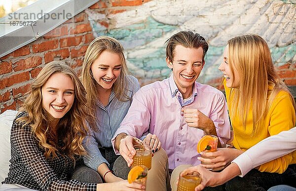 Gruppe von jungen glücklichen Menschen Freunde trinken Fruchtcocktails zusammen auf Haus Terrasse  lächelnd und lachend  Gruppe von Jugendlichen Ausdruck positiver Emotionen und Spaß haben auf der Party