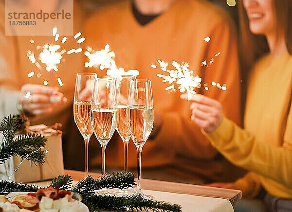 Gläser Champagner auf dem Tisch mit verschwommenen Hintergrund von festlichen Lichtern und eleganten Menschen Hände halten Weihnachten funkelt  Panoramablick von Freunden feiern Silvester oder Geburtstag mit Glück
