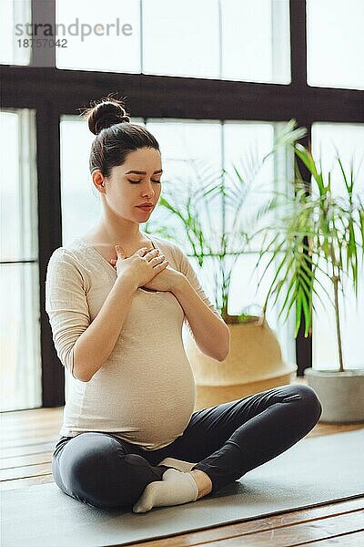 Meditation während der Schwangerschaft. Junge ruhige ruhige schwangere Frau macht Yoga zu Hause  meditieren und üben Achtsamkeit  werdende Mutter sitzt im Lotussitz mit geschlossenen Augen