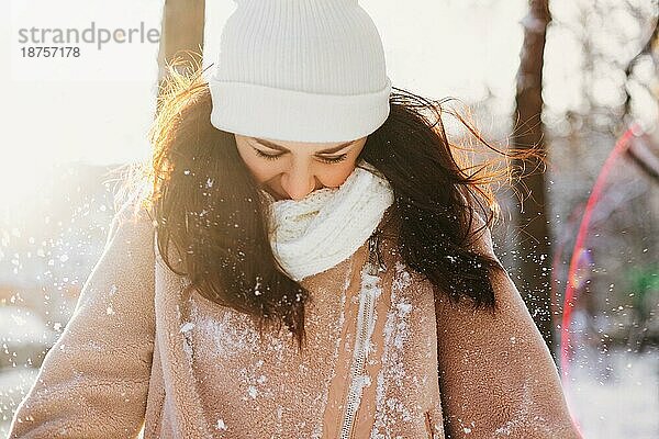 Optimistische junge Frau mit warmer Mütze auf den Augen lächelt  während sie auf der Straße an einem sonnigen Wintertag Spaß hat