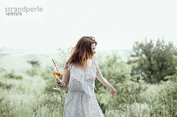 Junge Frau trinkt Alkoholcocktail mit Orange auf unscharfem Hintergrund der Natur