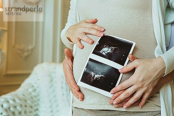 Familienplanung. Cropped Schuss der liebevollen Ehemann umarmt seine schwangere Frau hält Ultraschall Scan in den Händen  Mann und Frau in Erwartung des Wartens auf neue Baby zu Hause. Schwangerschaft Konzept