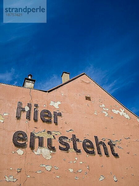 Hier entsteht - Ankündigung für ein Bauprojekt auf einer lachsfarbenen Hausmauer