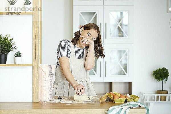 Glückliche Hausfrau mit rohem Teig beim Kochen am Tisch in der Küche