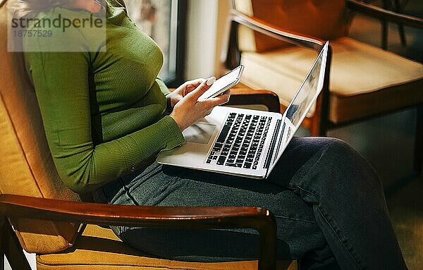 Seitenansicht einer glücklichen Frau  die lächelt und auf ihrem Laptop surft  während sie am Tisch sitzt und an einem Fernprojekt in der Cafeteria arbeitet