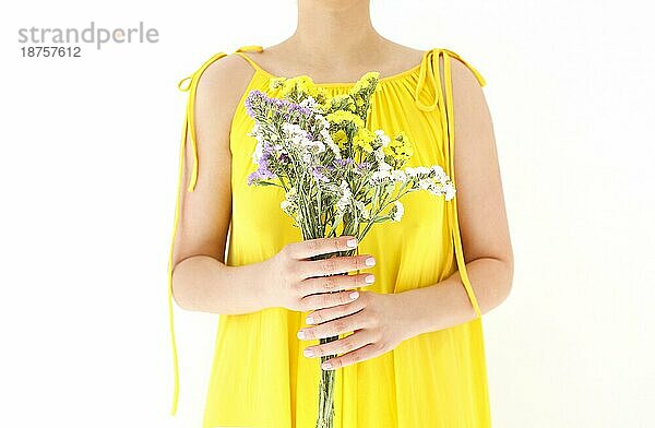 Unerkennbare Frau in gelbem Kleid versteckt sich hinter einem Strauß Wildblumen an einem Sommertag vor weißem Hintergrund