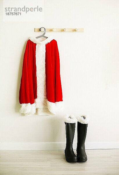 Santa Claus Kostüm hängt auf hölzernen Wand in der Nähe von Schuhen in hellen Raum. Saison celebraion cincept. Winterurlaub