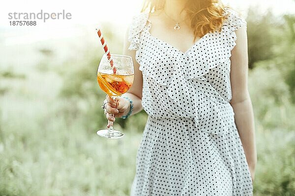 Junge Frau trinkt Alkoholcocktail mit Orange auf unscharfem Hintergrund der Natur