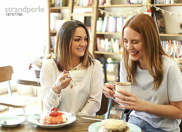 Glückliche junge multirassische Freundinnen sitzen am Tisch mit Pfannkuchen und Kaffee auf der Terrasse eines Cafés während der Mittagszeit