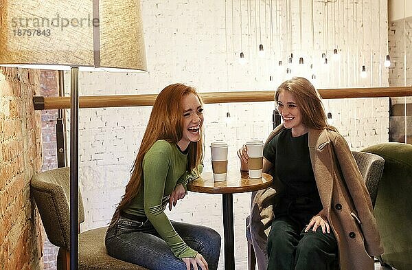 Multiethnische junge Frauen sitzen am Tisch und trinken ein heißes Getränk  während sie sich in einer gemütlichen Cafeteria am Wochenende ausruhen