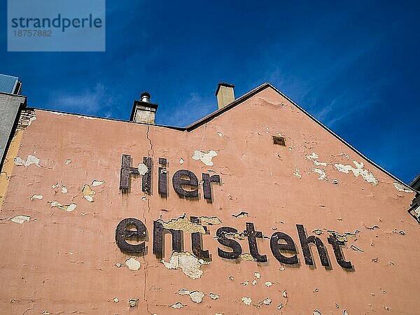 Hier entsteht - Ankündigung für ein Bauprojekt auf einer lachsfarbenen Hausmauer