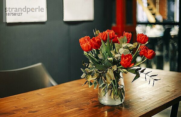 Closeup Foto von Strauß frischer roter Tulpen in Glasvase auf Holztisch im Wohnzimmer Interieur Hintergrund. Frische Schnittblumen für drinnen Dekoration. Florales Arrangement Konzept