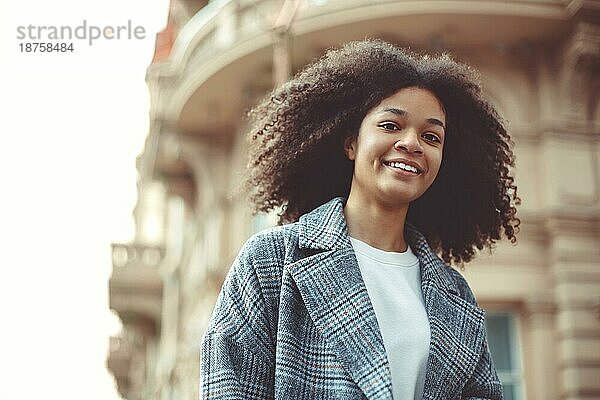 Junge stilvolle positive afroamerikanische Frau überqueren Zebrastreifen und lächelnd in die Kamera beim Gehen in der Stadt auf Herbsttag. Glückliches schwarzes Mädchen auf dem Zebrastreifen im Freien. Menschen auf den Straßen der Stadt