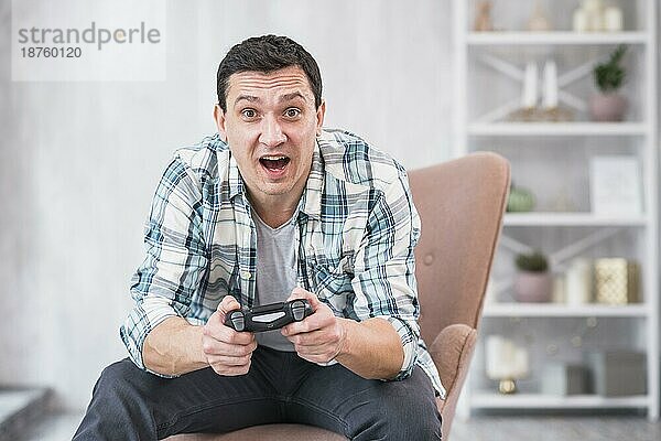 Aufgeregter junger Männchen im Sessel sitzend und mit Gamepad spielend