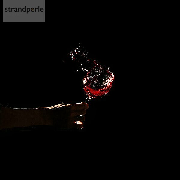 Person s Hand hält Glas Rotwein spritzt aus Glas. Foto mit hoher Auflösung