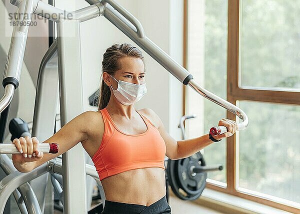 Frau im Fitnessstudio bei Übungen mit medizinischer Maske