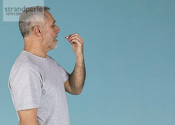 Seitenansicht kranker Mann nimmt Kapsel vor blauem Hintergrund
