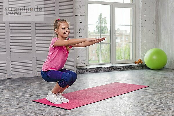 Lächelndes Mädchen hockt und trainiert eine rosa Matte