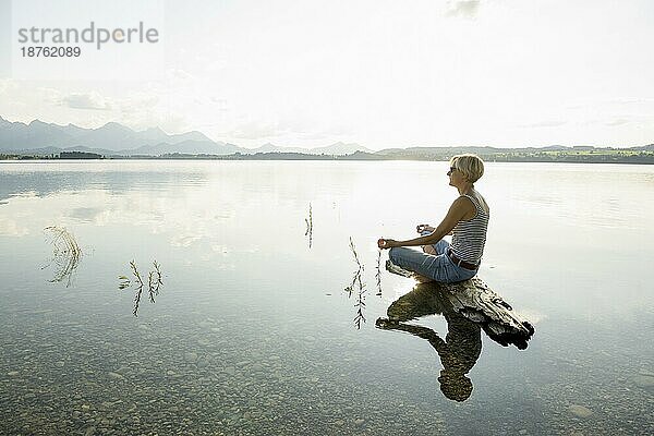 Entspannt auf einem Stein sitzende Frau  Forggensee  bei Füssen  Ostallgäu  Allgäu  Schwaben  Oberbayern  Bayern  Deutschland  Europa