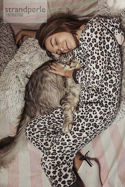 Mädchen im Schlafanzug umarmt ihre Katze im Bett