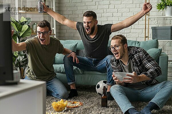 Vorderansicht fröhliche männliche Freunde  die zusammen Sportfernsehen schauen  während sie Snacks und Bier trinken. Foto mit hoher Auflösung