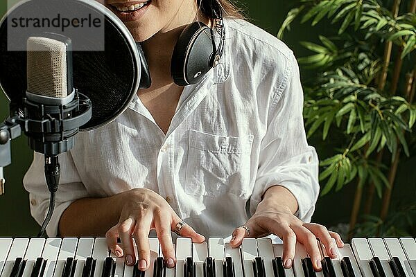 Lächelnde Musikerin  die drinnen auf der Klaviertastatur spielt und ins Mikrofon singt. Foto mit hoher Auflösung