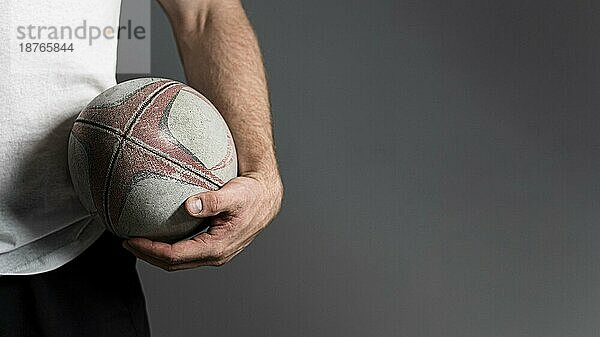 Vorderansicht männlicher Rugbyspieler  der den Ball in der Hüfte hält  mit Kopierraum. Schönes Foto