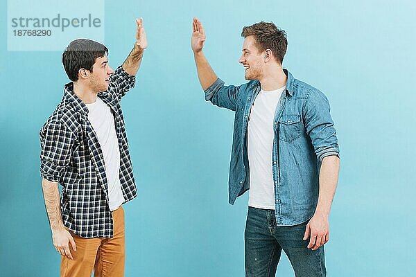 Junger männlicher Freund gibt High Five vor blauem Hintergrund. Foto mit hoher Auflösung