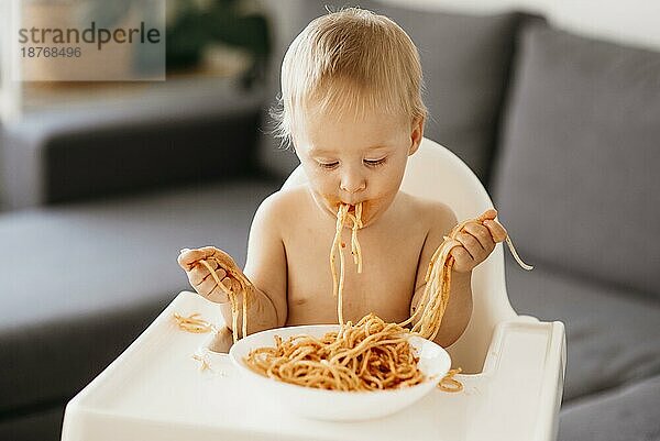 Vorderansicht Baby Junge spielt mit Nudeln seinen Hochstuhl. Hohe Auflösung Foto