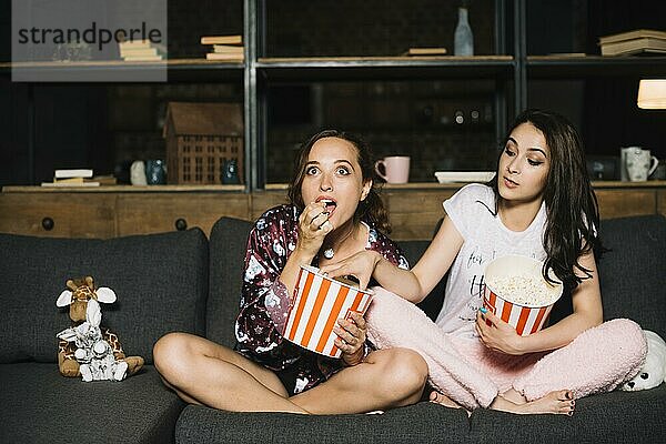 Frau sieht sich einen Film an  während ihre Freundin Popcorn aus ihrem Eimer nimmt