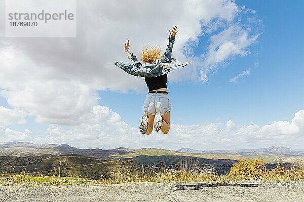 Frau springt vor Freude auf einem Hügel. Foto mit hoher Auflösung