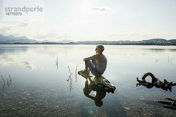 Entspannt auf einem Stein sitzende Frau  Forggensee  bei Füssen  Ostallgäu  Allgäu  Schwaben  Oberbayern  Bayern  Deutschland  Europa