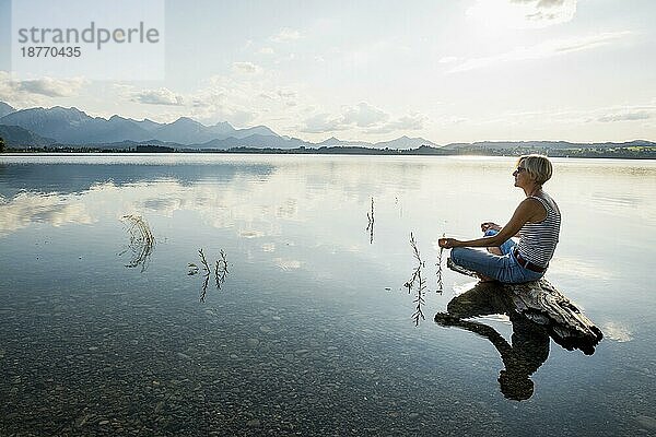 Entspannt auf einem Stein sitzende Frau  Forggensee  bei Füssen  Ostallgäu  Allgäu  Schwaben  Oberbayern  Bayern  Deutschland  Europa