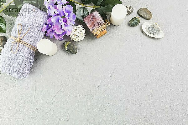 Erhöhte Ansicht Handtuch Kerzen Peeling Flasche Blumen Spa Steine grau Hintergrund. Foto mit hoher Auflösung