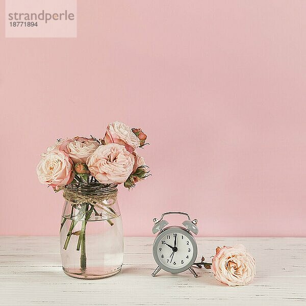 Rosen Vase in der Nähe Wecker hölzernen Schreibtisch gegen rosa Hintergrund. Hohe Auflösung Foto