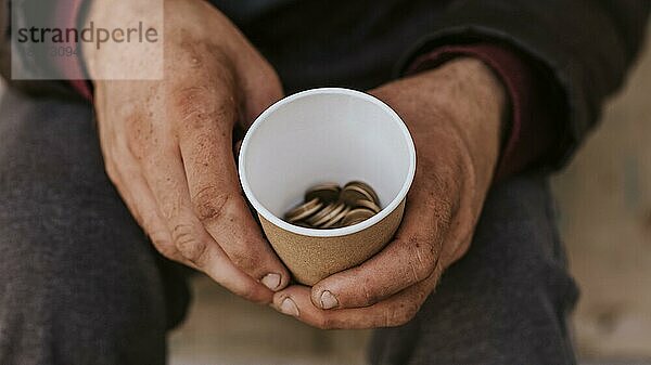 Vorderansicht Obdachloser  der eine Tasse mit Münzen hält