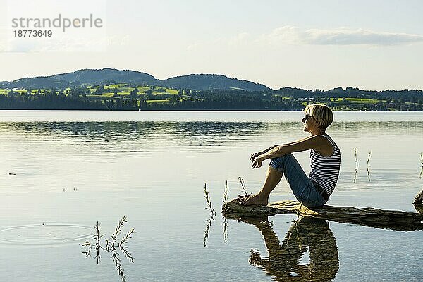 Entspannt auf einem Stein sitzende Frau  Forggensee  bei Füssen  Ostallgäu  Allgäu  Schwaben  Oberbayern  Bayern  Deutschland  Europa