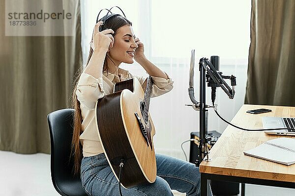 Seitenansicht weiblichen Musiker setzen Kopfhörer Rekord Song spielen akustische Gitarre. Foto mit hoher Auflösung