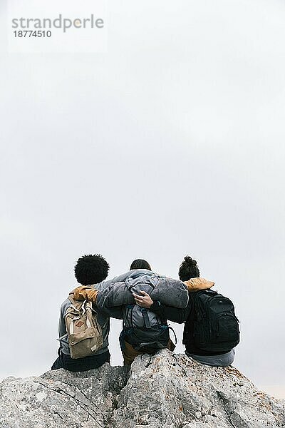 Drei Freunde mit ihren Armen um sitzende Bergspitze. Foto mit hoher Auflösung