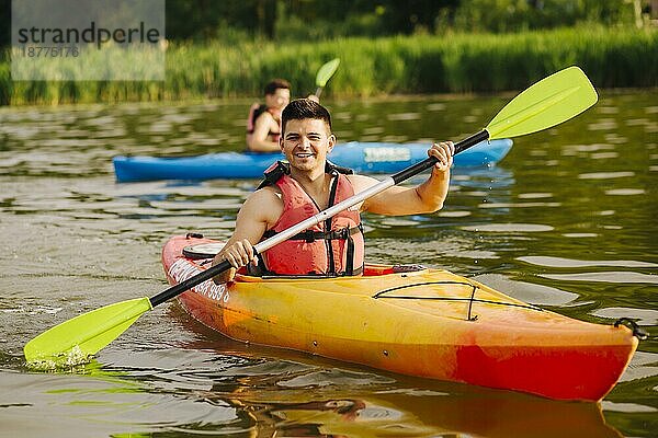 Lächelnder Mann paddelt Kajak auf dem See. Foto mit hoher Auflösung