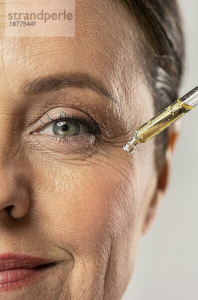 Lächelnde ältere Frau benutzt Serum für ihre Augenfalten