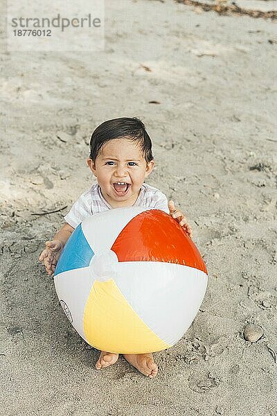 Kind im Sand sitzend mit aufblasbarem Ball
