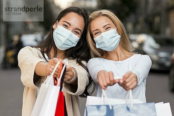 Zwei Frauen mit medizinischen Masken posieren zusammen mit Einkaufstüten