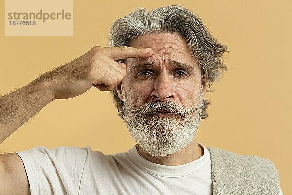 Vorderansicht älterer Mann mit Bart  der auf Falten zeigt