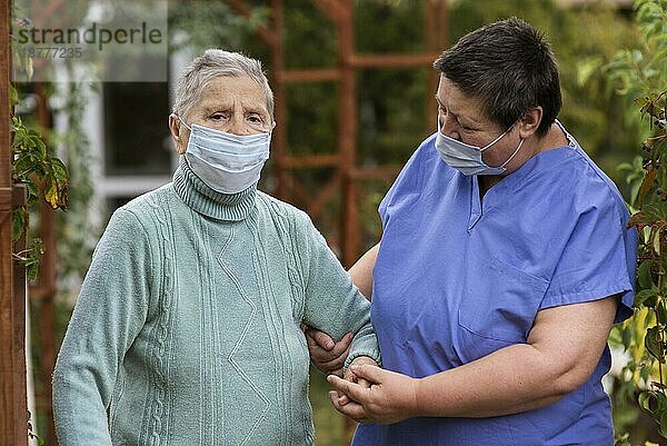 Krankenschwester kümmert sich um ältere Frau mit medizinischer Maske