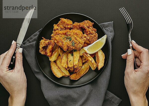 Draufsicht auf einen Fish-Chips-Teller mit einer Frau  die das Besteck hält. Schönes Foto