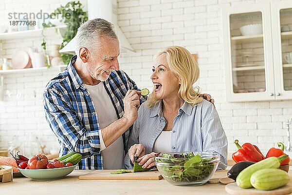 Senior Mann füttert Gurkenscheibe ihre Frau Küche