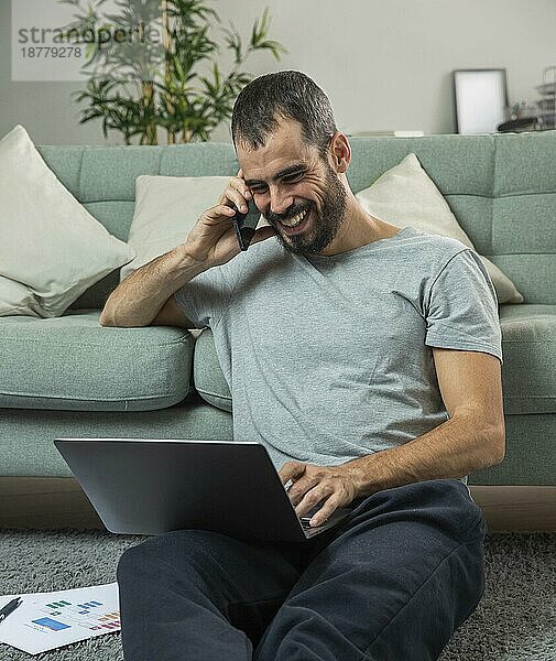 Lächelnder Mann telefoniert zu Hause und arbeitet am Laptop